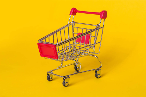 Prázdný nákupní vozík na žlutém podkladu. Obchod košík pro výrobky. - Fotografie, Obrázek