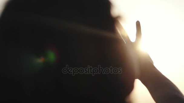 女の子は彼女の手を太陽に見えます。女の子は、日没で安静です。梨花は、太陽の光で手します。太陽に手を振ってください。 - 映像、動画