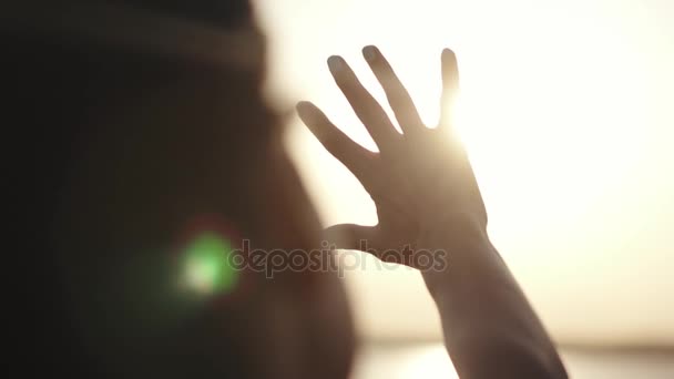 女の子は彼女の手を太陽に見えます。女の子は、日没で安静です。梨花は、太陽の光で手します。太陽に手を振ってください。 - 映像、動画