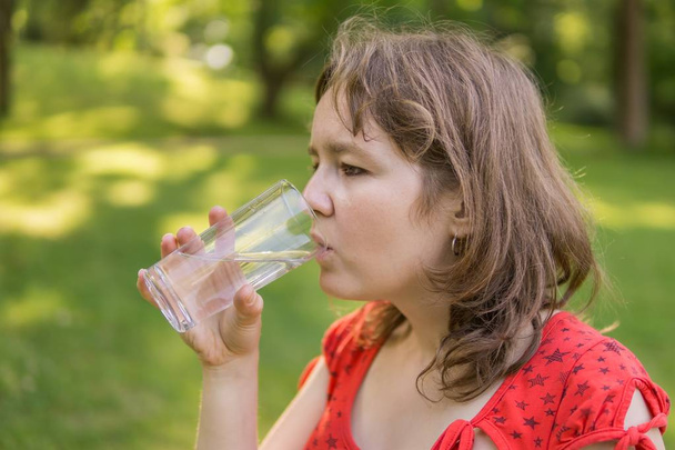 Νεαρή γυναίκα είναι πόσιμο νερό από το ποτήρι στη φύση στο sunny ζεστό  - Φωτογραφία, εικόνα