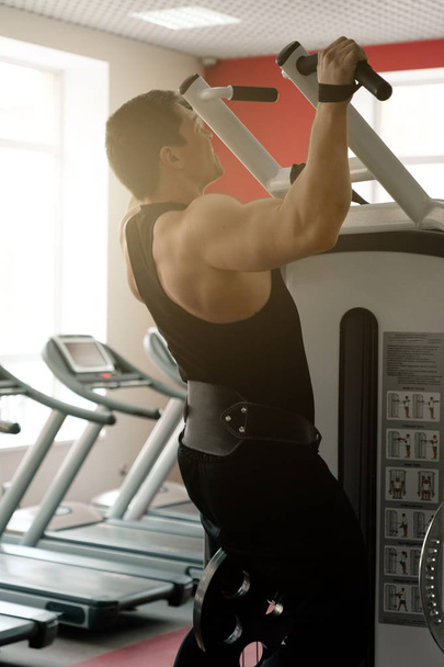 A man in a black t-shirt and pants with a weightlifting belt is tightened on the treadmill, side view - Фото, изображение