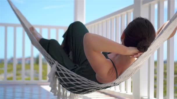 Widok z tyłu z młodą kobietą spędzić słoneczny dzień w hamaku na jej tarasie - Materiał filmowy, wideo