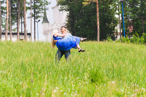 Młody człowiek, niosąc swoją dziewczynę w ramiona na boisko. Para zabawy w naturze w letni dzień. - Zdjęcie, obraz