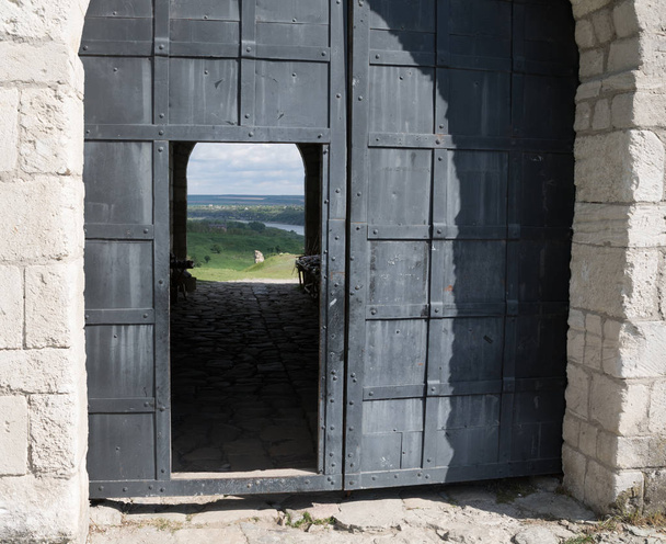 Door in old metal castle gates. Tunnel corridor with arch into green landscape - Photo, Image