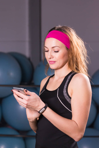 Sport, Fitness, Technik und People-Konzept - junge Frau mit Aktivitätstracker und Smartphone im Fitnessstudio - Foto, Bild