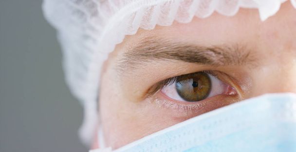 A portrait of a doctor or surgeon in a medical mask, a respirator, brown eyes, a surgical cap, in a hospital or a clinic. - 写真・画像
