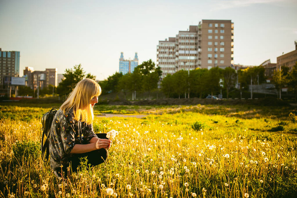 Young blonde girl in dress with shoulder bag, walking on dandelion field - Fotó, kép