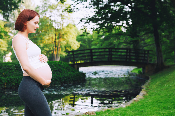 Pregnant woman holds hands on belly on nature background - Photo, Image