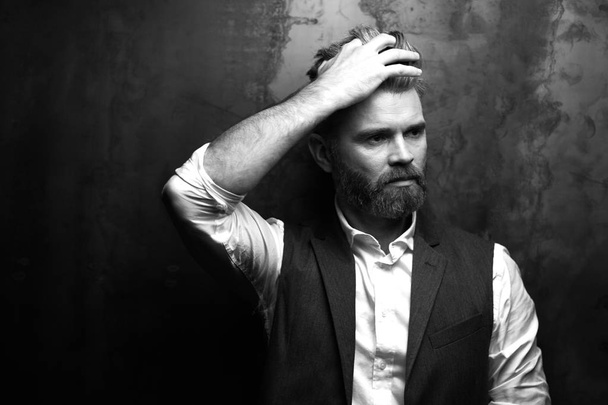 Handsome beautiful serious man with beard, wearing white shirt and black waistcoat, posing in studio on dark grey background in black and white - Photo, image