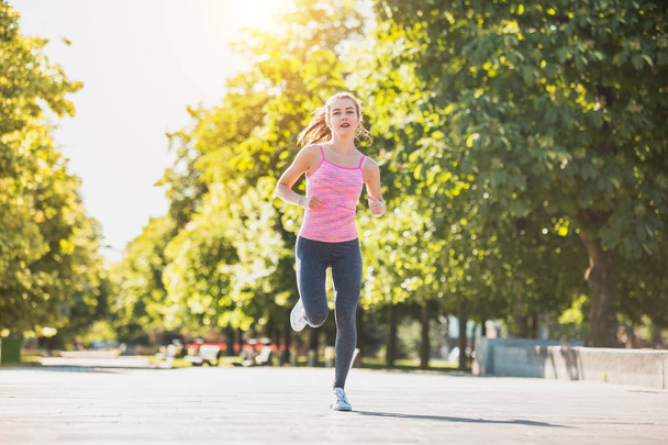 Ziemlich sportliche Frau joggt im Sonnenaufgangslicht im Park - Foto, Bild