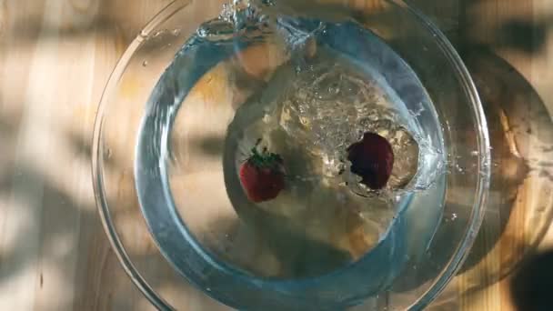 reife frische Erdbeeren, die an einer Schüssel auf einem Holztisch ins Wasser fallen. Zeitlupe Nahaufnahme von oben - Filmmaterial, Video