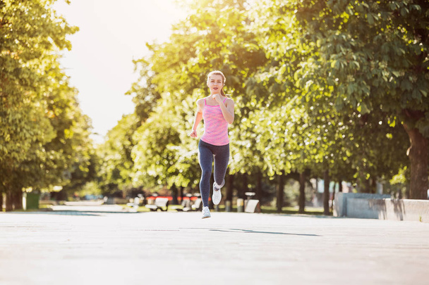 Pretty sporty woman jogging at park in sunrise light - Photo, Image