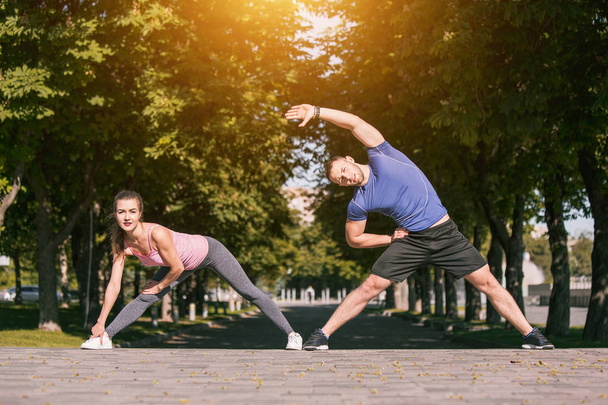 Fit fitness nainen ja mies tekee venyttely harjoituksia ulkona puistossa
 - Valokuva, kuva