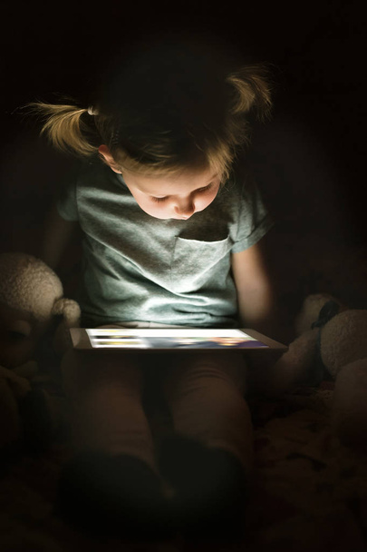 Little girl at home at night watching something on tablet. - Foto, imagen