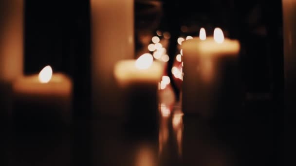 Warm white wax candles burning on floor of dark room - Footage, Video