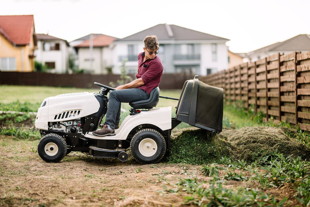 Gardner trimming and unloading cut grass from the garden using a ride on lawn mower - Φωτογραφία, εικόνα
