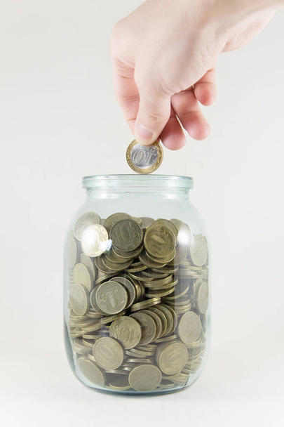 Glass jar with money on a white background. Hand with a coin - Fotografie, Obrázek