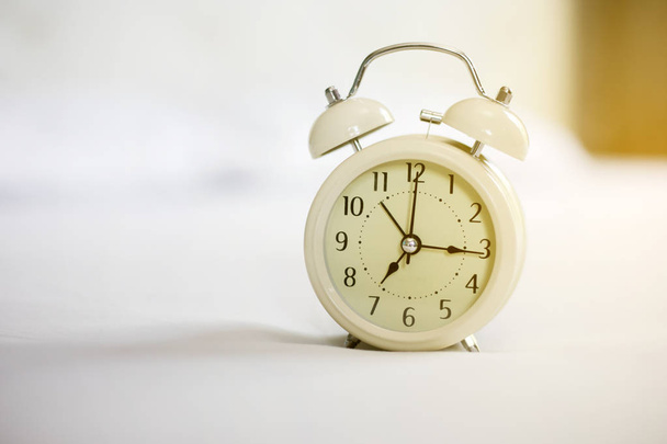 Reloj despertador analógico en cama blanca, hora en la mañana con un calabozo
 - Foto, Imagen
