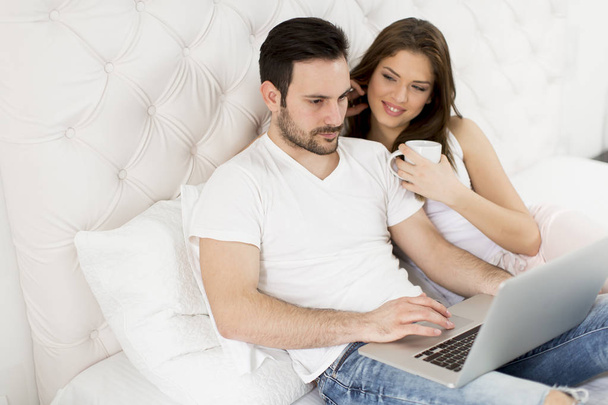 Alegre pareja usando un portátil acostado en su cama en casa
 - Foto, Imagen