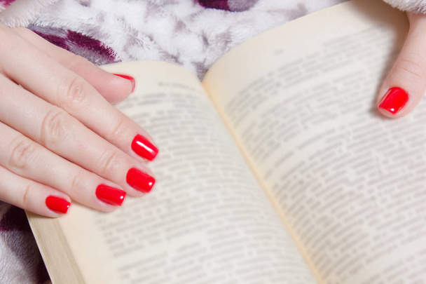 χέρι περιποιημένα γυναίκα με τα κόκκινα νύχια και βιβλίο - Φωτογραφία, εικόνα