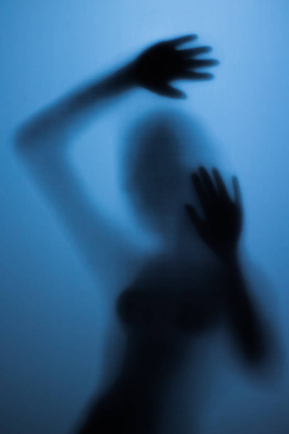 Spaventosa silhouette di una ragazza dietro un vetro in bagno. Spaventosa ragazza dietro la porta di vetro nella luce blu
 - Foto, immagini