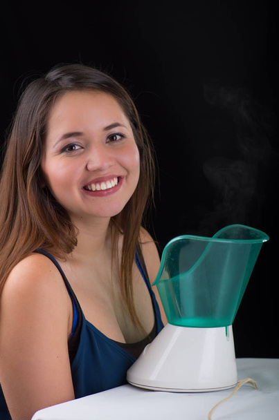 Young woman posing for camera behind of a medical vaporizer nebulizer machine on black background - Photo, image