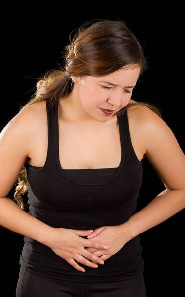 Beautiful young woman with stomach ache or nausea in a black background - Foto, Imagen