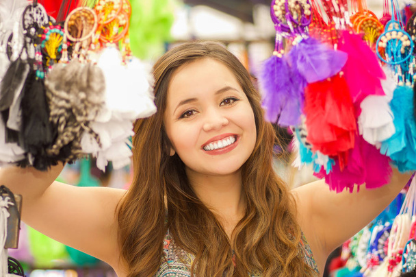 Close up of a beautiful smiling young woman hiding behind a colorful catchdreamer, in colorful market fabrics background - Fotoğraf, Görsel