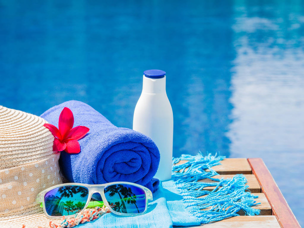 Flores vermelhas de frangipani (plumeria), óculos de sol, chapéu de praia, toalha azul e protetor solar ao lado da piscina. Férias, praia, conceito de viagem de verão
 - Foto, Imagem