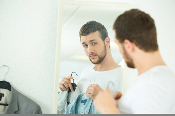 man looking in mirror comparing shirts - Photo, image