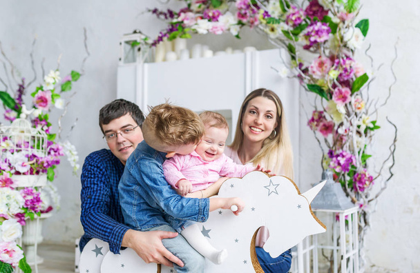 Família feliz de quatro sentar no quarto com flores e brincar com as crianças em seu cavalo de brinquedo de madeira
 - Foto, Imagem