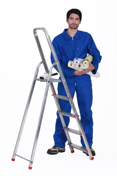 Man stood by ladder holding selection of wallpaper rolls - Foto, Imagem