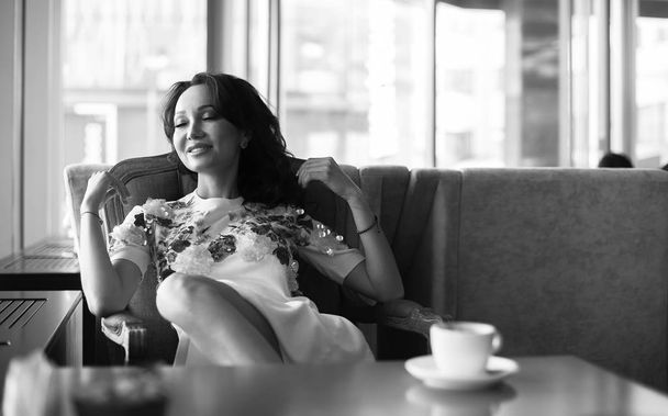 Nuori nainen juo kahvia ja käyttää älypuhelinta istuu sisällä kaupunkien kahvilassa. Cafe Cityn elämäntapa. Rento muotokuva kauniista tytöstä. Mustavalkoinen
 - Valokuva, kuva