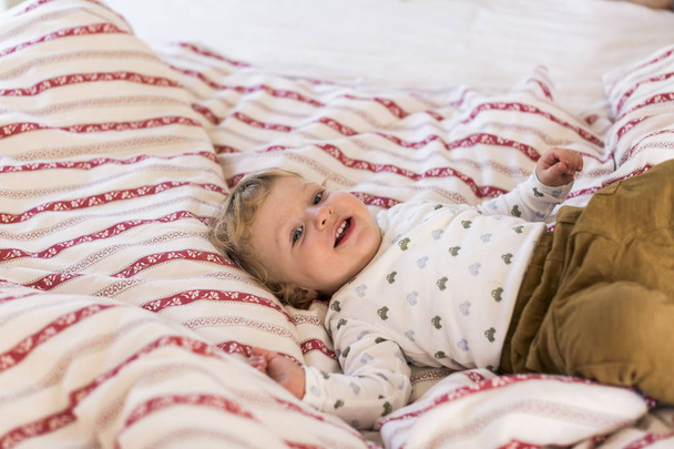 Cute little boy at home lying on bed smiling. - 写真・画像