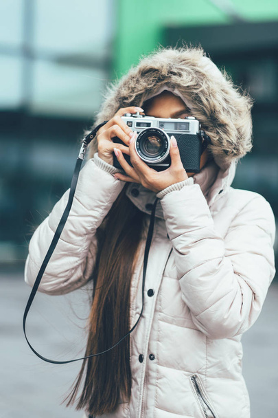 ヴィンテージ レトロなフィルム カメラを使って外で撮影冬のコートで美しい少女。都市環境 - 写真・画像