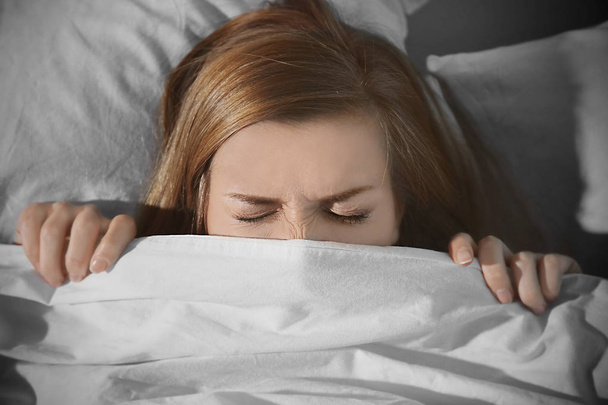 Young scared woman hiding under blanket while lying in bed at home - Foto, Bild