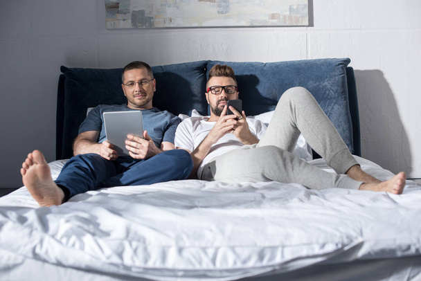 Homosexual couple using devices  - Фото, изображение