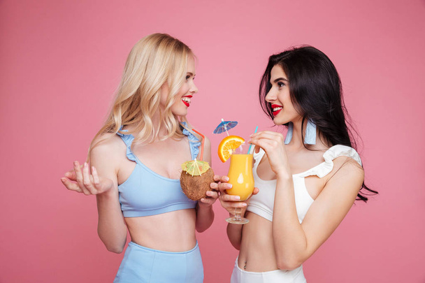 Smiling young two women dressed in swimwear drinking cocktails. - Foto, Imagem