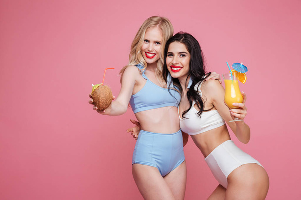 Happy young two ladies dressed in swimwear drinking cocktails. - Zdjęcie, obraz