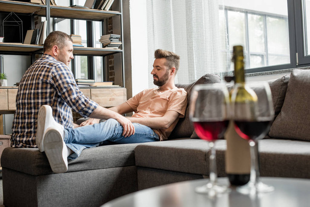 homosexual couple talking while sitting on sofa - Foto, imagen