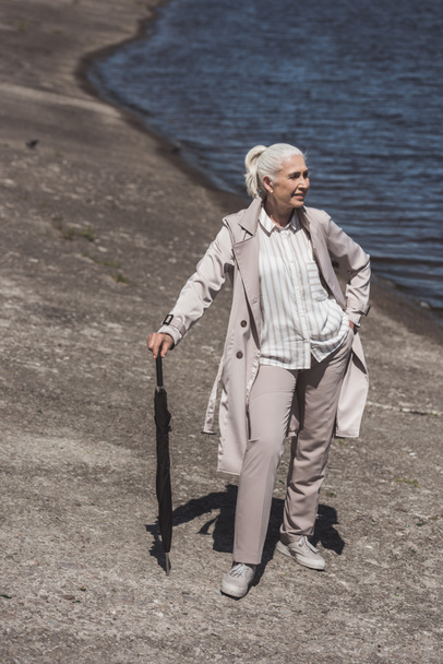 senior woman posing with umbrella on riverside - Фото, изображение