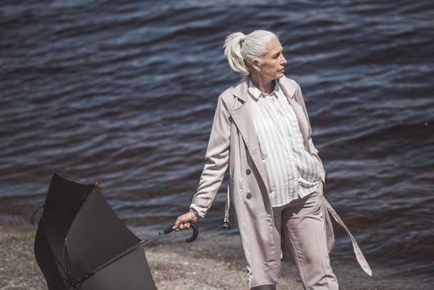vrouw met paraplu op de kust rond de rivier lopen - Foto, afbeelding
