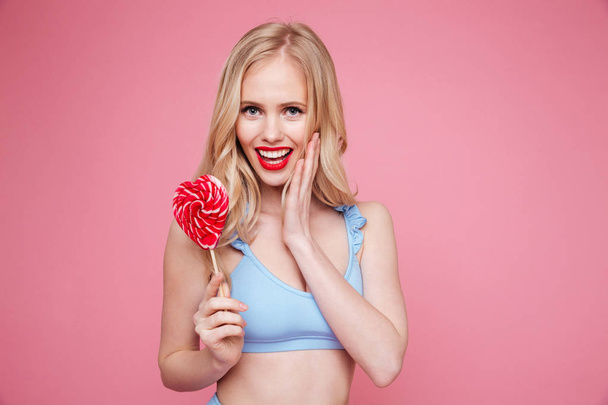 Cute blonde woman in swimsuit posing with heart shaped lollipop - Photo, Image
