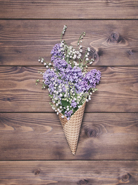 Waffle cone with lily valley and lilak flowers on wooden backgro - Фото, изображение