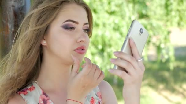 A young girl adjusts her makeup with a phone - Footage, Video