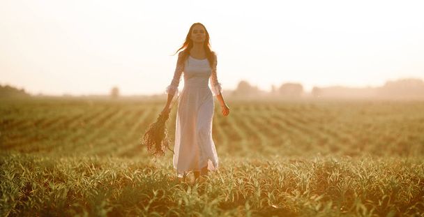 トウモロコシ畑の長い白いレースのドレスの若い女性.  - 写真・画像