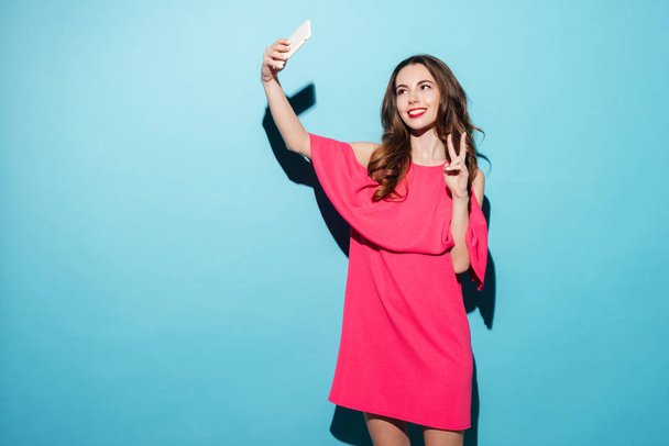 Młoda kobieta w sukni podejmowania selfie i pokazuje gest pokoju - Zdjęcie, obraz