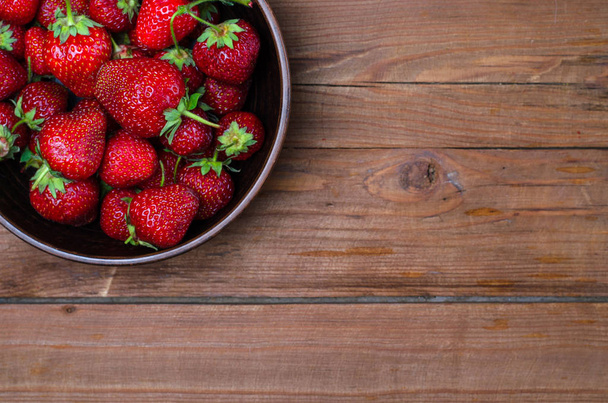 Ripe red strawberries in a clay bowl on a wooden table, copy spa - Foto, Bild