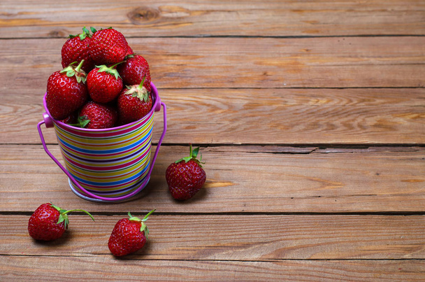 Ripe strawberries in a bright bucket on a wooden table, a copy o - Foto, Bild