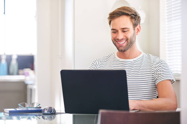 attractive man smiling at his laptop screen sitting at home - Foto, afbeelding